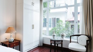 Ein Hotelzimmer mit großem Fenster, einem Nachttisch mit Lampe, einem Sessel und einer Ziervase.