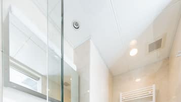 Un baño moderno con cabina de ducha de vidrio, un lavabo blanco y un inodoro.