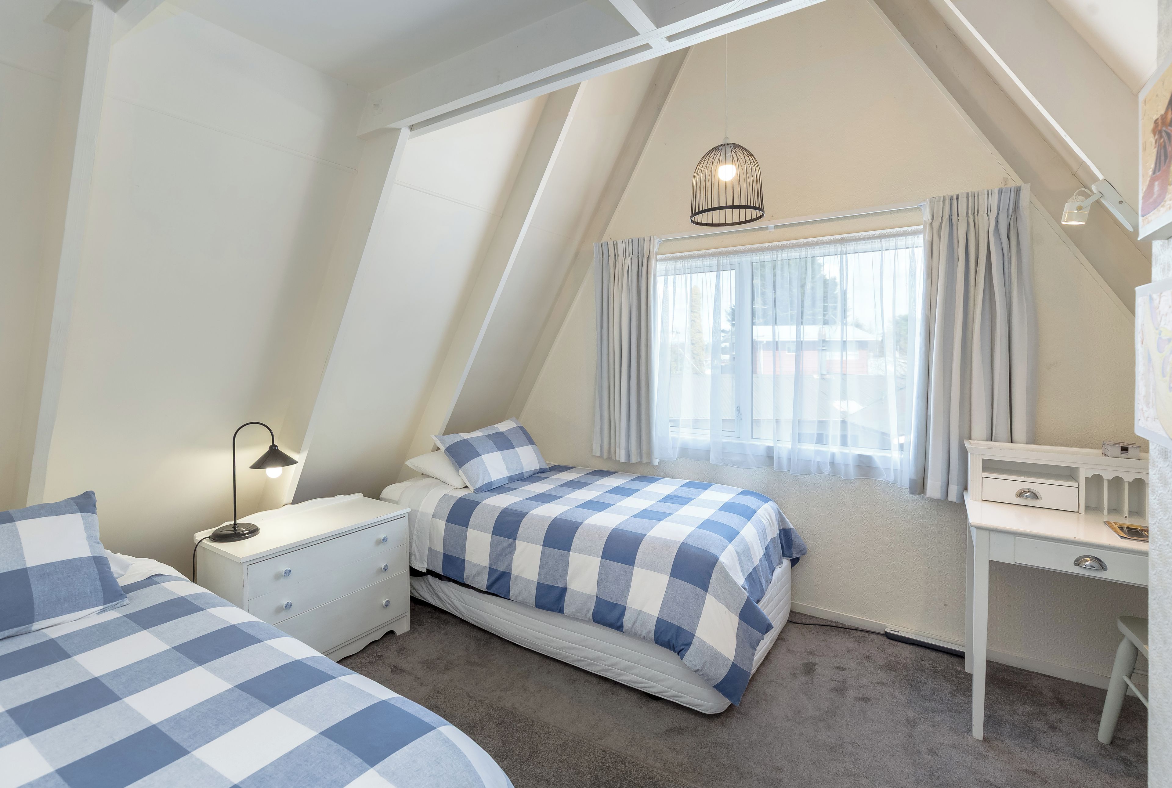 Quarto com cama, mesa de cabeceira, abajur e escrivaninha com cadeira.