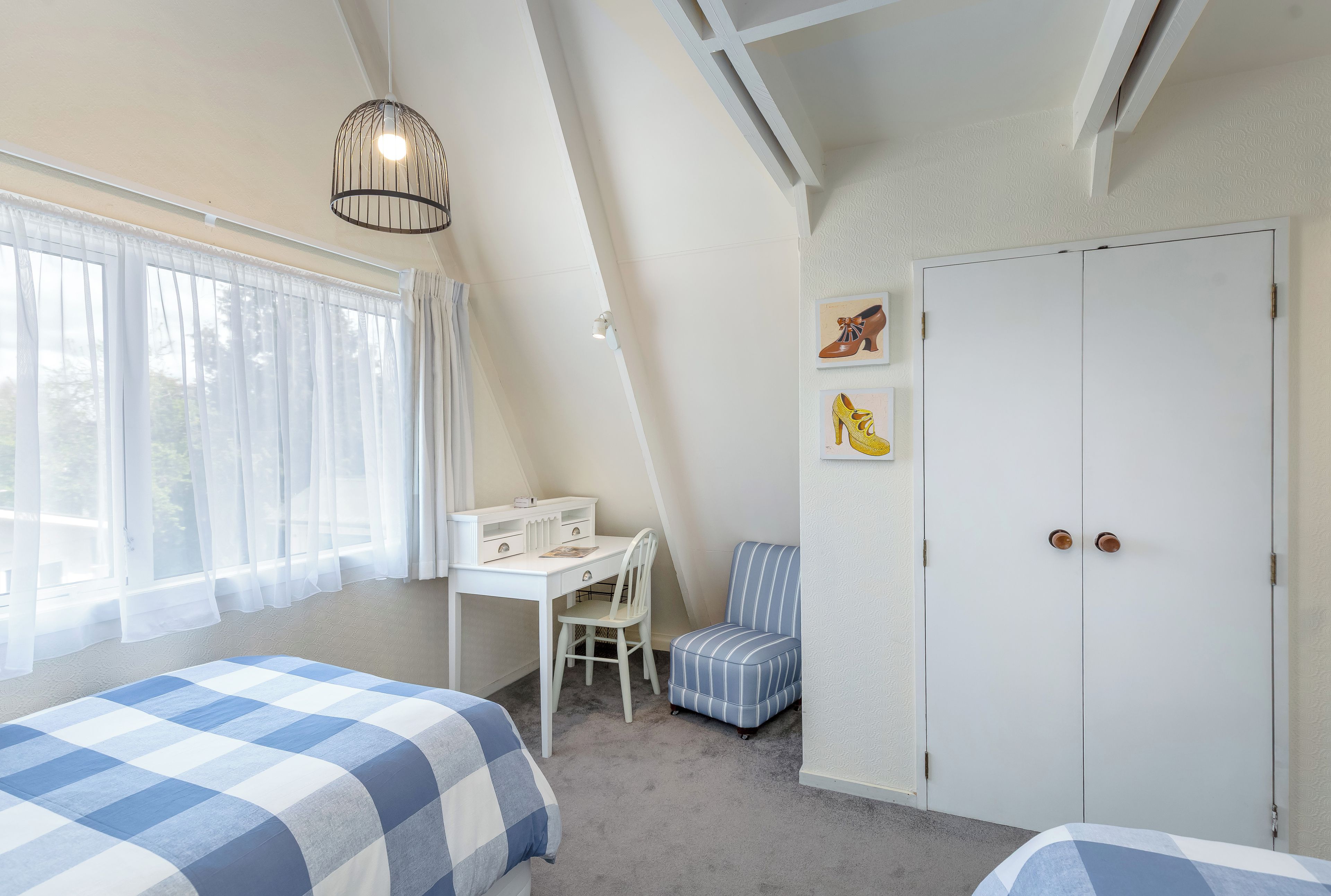Ein Schlafzimmer mit Schreibtisch, Stuhl, zwei Betten, einem Kleiderschrank und Bildern an der Wand.
