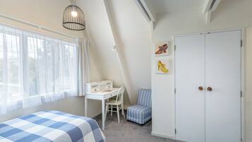 Ein Schlafzimmer mit Schreibtisch, Stuhl, zwei Betten, einem Kleiderschrank und Bildern an der Wand.