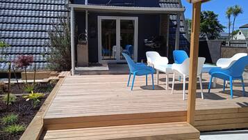 Een overdekt terras met houten trappen naar een zithoek met witte en blauwe stoelen.