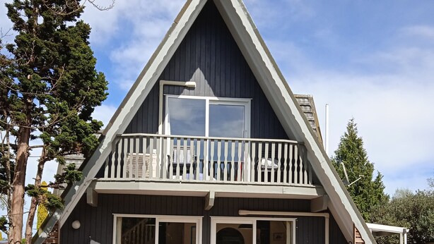 A two-story wooden cabin with a balcony, large sliding glass doors, and a deck area with outdoor furniture. - The house for all seasons, occasions and ages. Perfect for families! (Greytown)