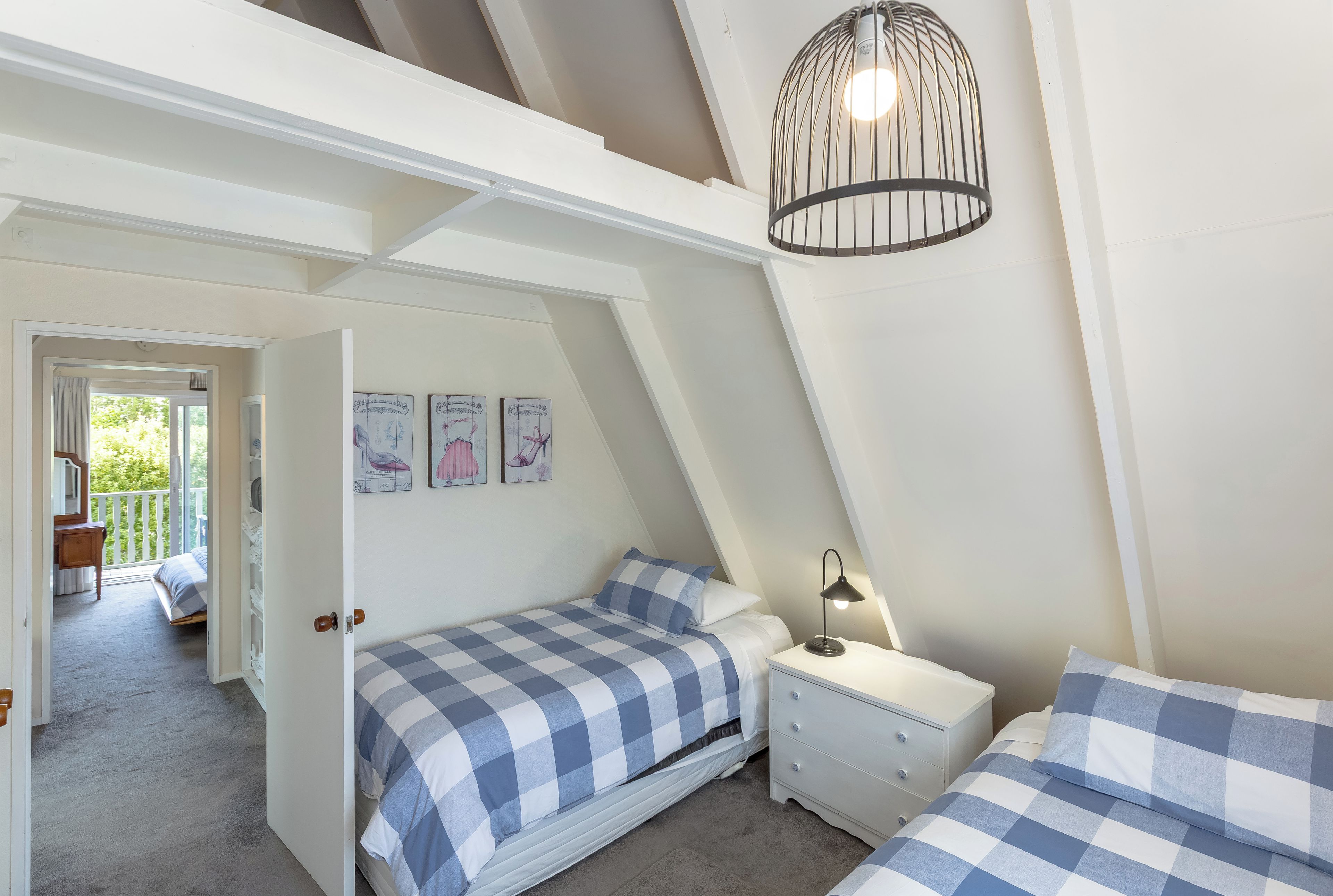 A bedroom with a sloped ceiling, a bed with checkered bedding, a bedside table with a lamp, and a door leading to a balcony.