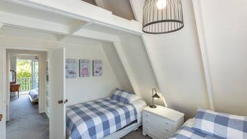 A bedroom with a sloped ceiling, a bed with checkered bedding, a bedside table with a lamp, and a door leading to a balcony.