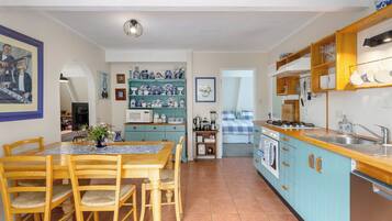 A kitchen with a dining area, featuring a table with chairs, a microwave, a stove, and various kitchen utensils.