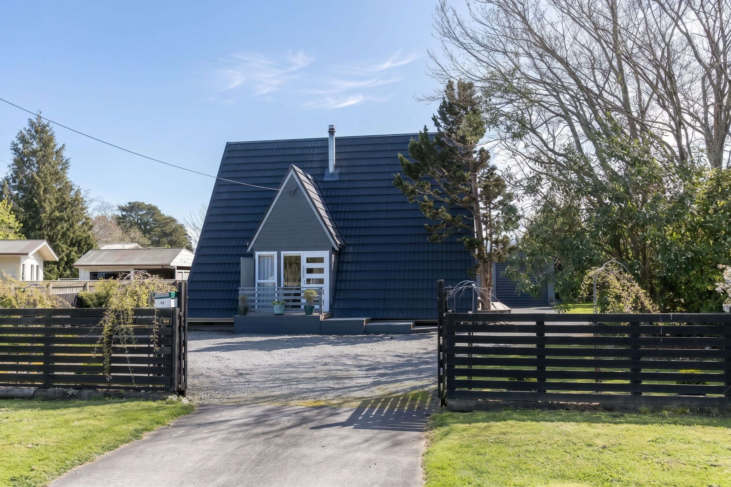 A house with a dark roof, a front porch, and a gravel driveway leading to a gated entrance.