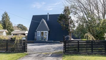 A house with a dark roof, a front porch, and a gravel driveway leading to a gated entrance.