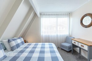 A bedroom with a checkered bed, a small table, a chair, and a window with sheer curtains. - The house for all seasons, occasions and ages. Perfect for families! (Greytown)