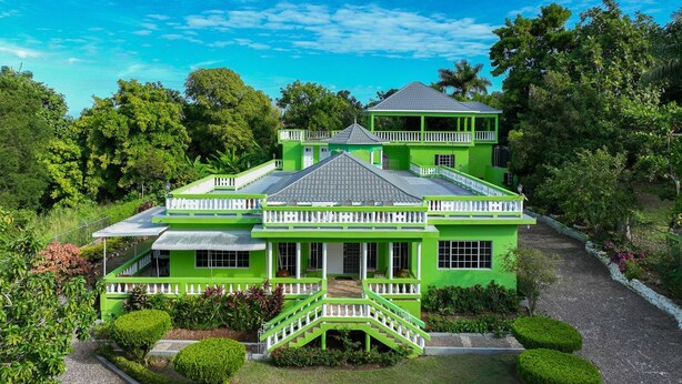 A large, two-story house with a green exterior and white trim, surrounded by lush greenery and a gravel driveway. - Bungalow on the Terrace Coral Gardens<br>Montego Bay (Montego Bay)