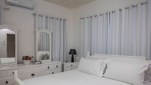 A white bedroom with a large bed, a dresser with drawers, a mirror, a bedside table with a lamp, and a window with curtains. - Bungalow on the Terrace Coral Gardens<br>Montego Bay (Montego Bay)
