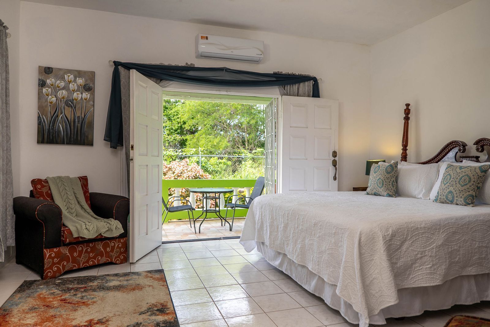 A bedroom with a bed, a chair, a table, and an open door leading to a balcony.