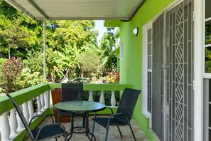 Un espacio de estar techado al aire libre con una mesa y sillas, rodeado de exuberante vegetación y una barandilla blanca.