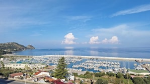Ein Yachthafen mit vielen vertäuten Booten, im Hintergrund eine Küstenstadt und ein klarer Himmel.