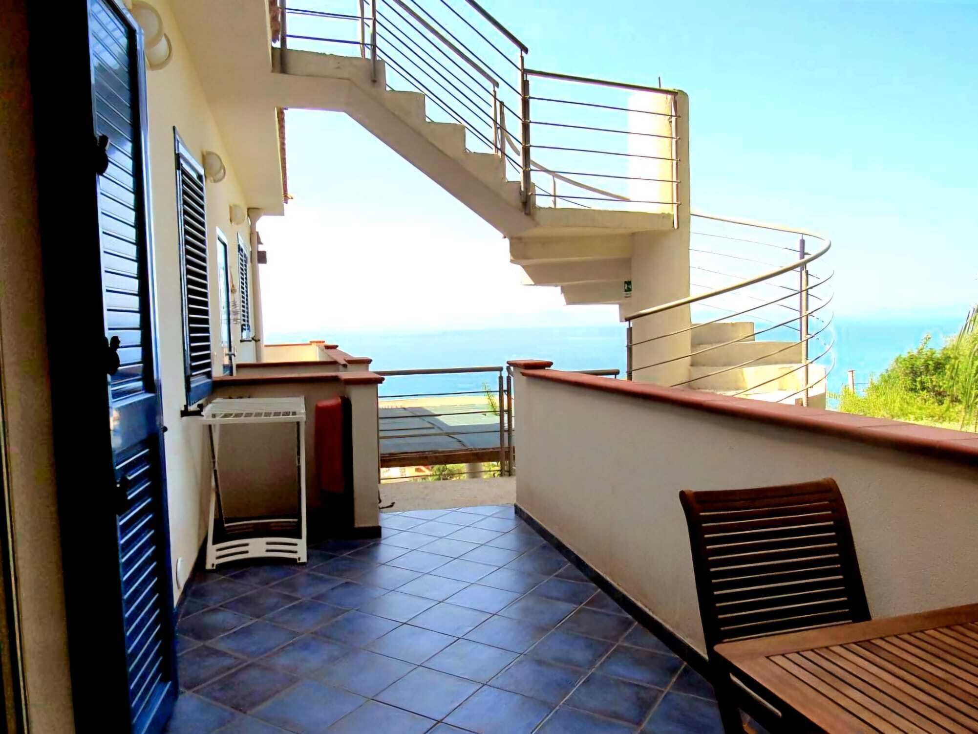 Un balcon avec vue sur la mer, un escalier et un petit coin salon.