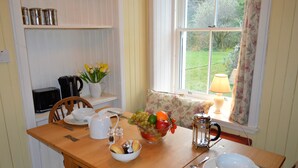 A dining table set with a bowl of fruit, a coffee pot, and a pitcher. - Quiet village location in beautiful valley close to Dunoon, Argyll. Sleeps 2, pet friendly (Strachur)