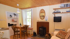 A cozy living room with a fireplace, wooden furniture, and a television mounted on the wall. - Quiet village location in beautiful valley close to Dunoon, Argyll. Sleeps 2, pet friendly (Strachur)
