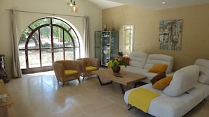 A spacious living room with a large arched window, a sofa, two armchairs, a coffee table, and a painting on the wall. - House / Villa - Gordes (Gordes)