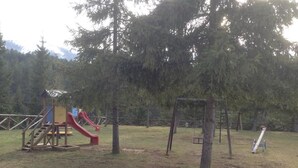 Une aire de jeux extérieure avec un toboggan rouge et des balançoires.