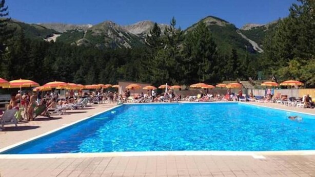 Une piscine entourée de montagnes et d’arbres, avec des chaises longues et des parasols.