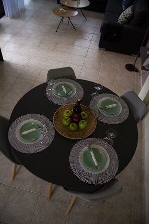 Enjoy meals with friends and family at this dining area, featuring a round table for four, complete with plates, napkins, and a wine and fruit basket.