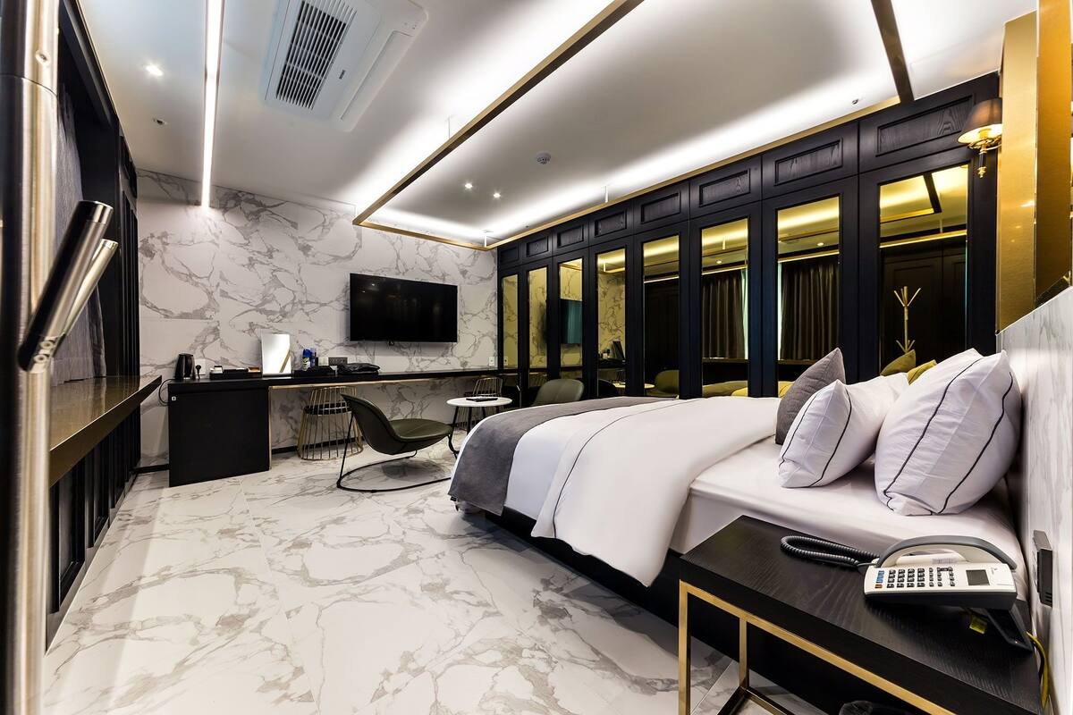 A modern hotel room with a large bed, a desk with a chair, a TV, and a bathroom with a mirror and vanity.