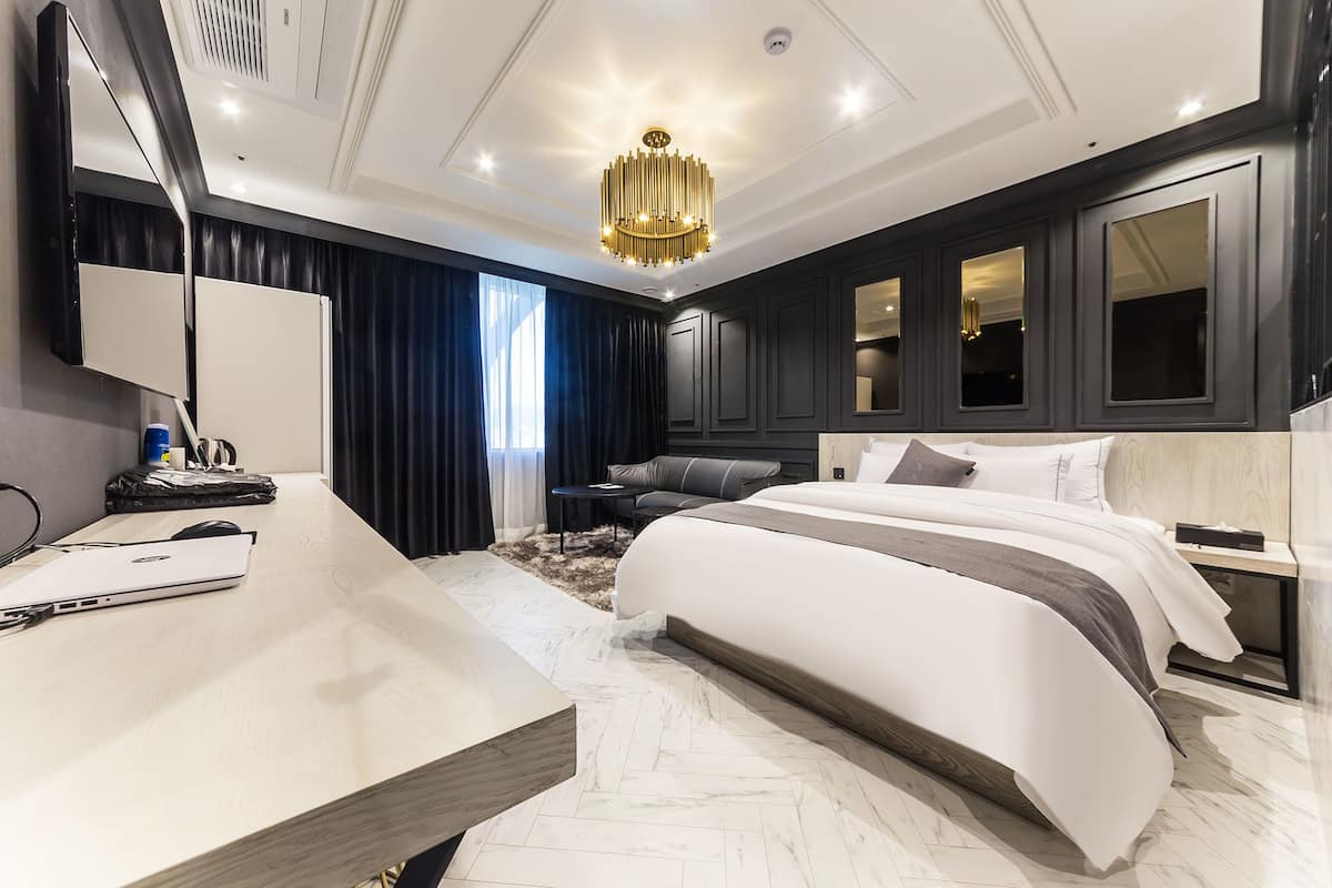 A modern hotel room with a large bed, a desk with a laptop, a desk lamp, and a large mirror.