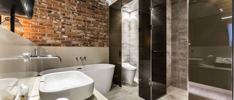 A modern bathroom with a brick wall, a freestanding bathtub, a glass-enclosed shower, and a vanity with a sink and towel.
