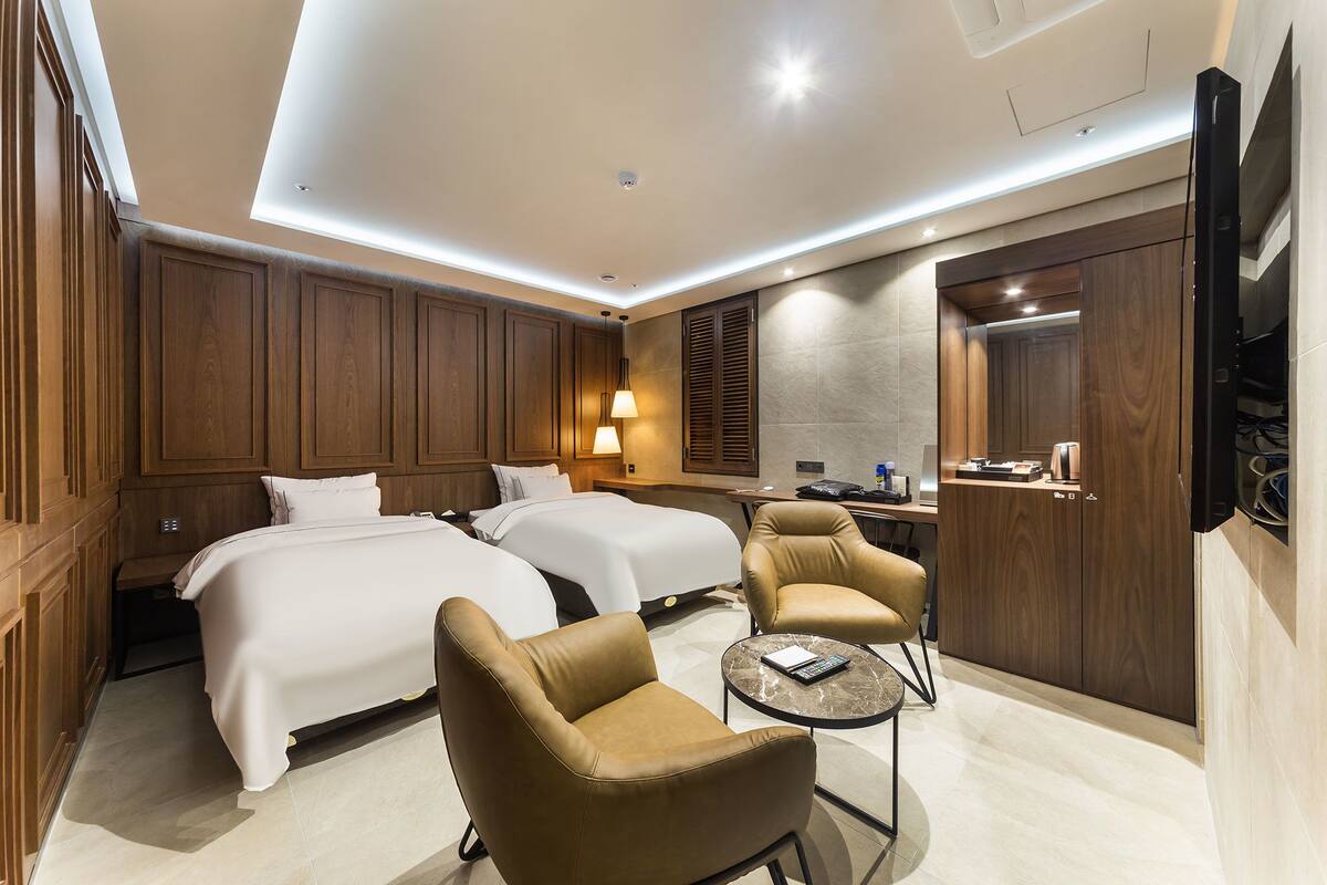 A hotel room with two beds, a sitting area with chairs, a small table, a TV, and a wardrobe.