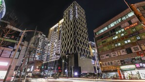 A modern building with a unique geometric facade, surrounded by other high-rise buildings and street lights. - Yongin Astro Hotel (Yongin)