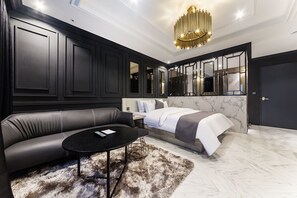 A modern bedroom with a black leather sofa, a round black coffee table, a fluffy rug, a bed with white bedding, and a large mirror. - Yongin Astro Hotel (Yongin)