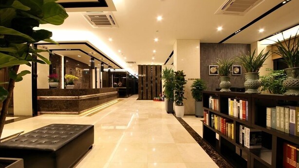Un hall d’hôtel comprenant un comptoir d’accueil, un espace salon et une bibliothèque remplie de livres.