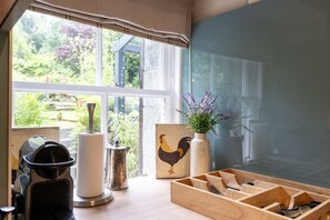 A kitchen with a window, a coffee machine, a kettle, a vase with flowers, a wooden utensil holder, and a rooster painting. - Seaview location in Inverarary, historic cottage within walking distance of town centre, sleeps 4 (Inverarary)