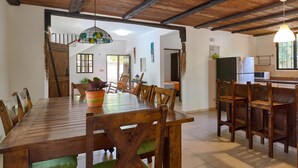 A wooden dining table with chairs, a kitchen area with a refrigerator and microwave, and a staircase leading to another room. - Villa Bayacanes (La Vega)