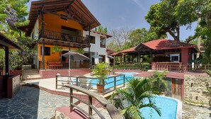 A resort with a swimming pool, wooden deck, and a two-story building with balconies. - Villa Bayacanes (La Vega)