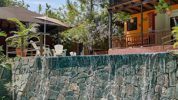 A swimming pool with a stone wall, white lounge chairs, and a building with a balcony. - Villa Bayacanes (La Vega)