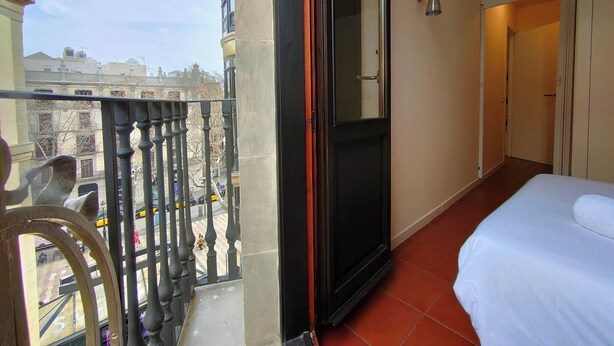 A hotel room with a balcony, a bed, a door, and a view of the cityscape.