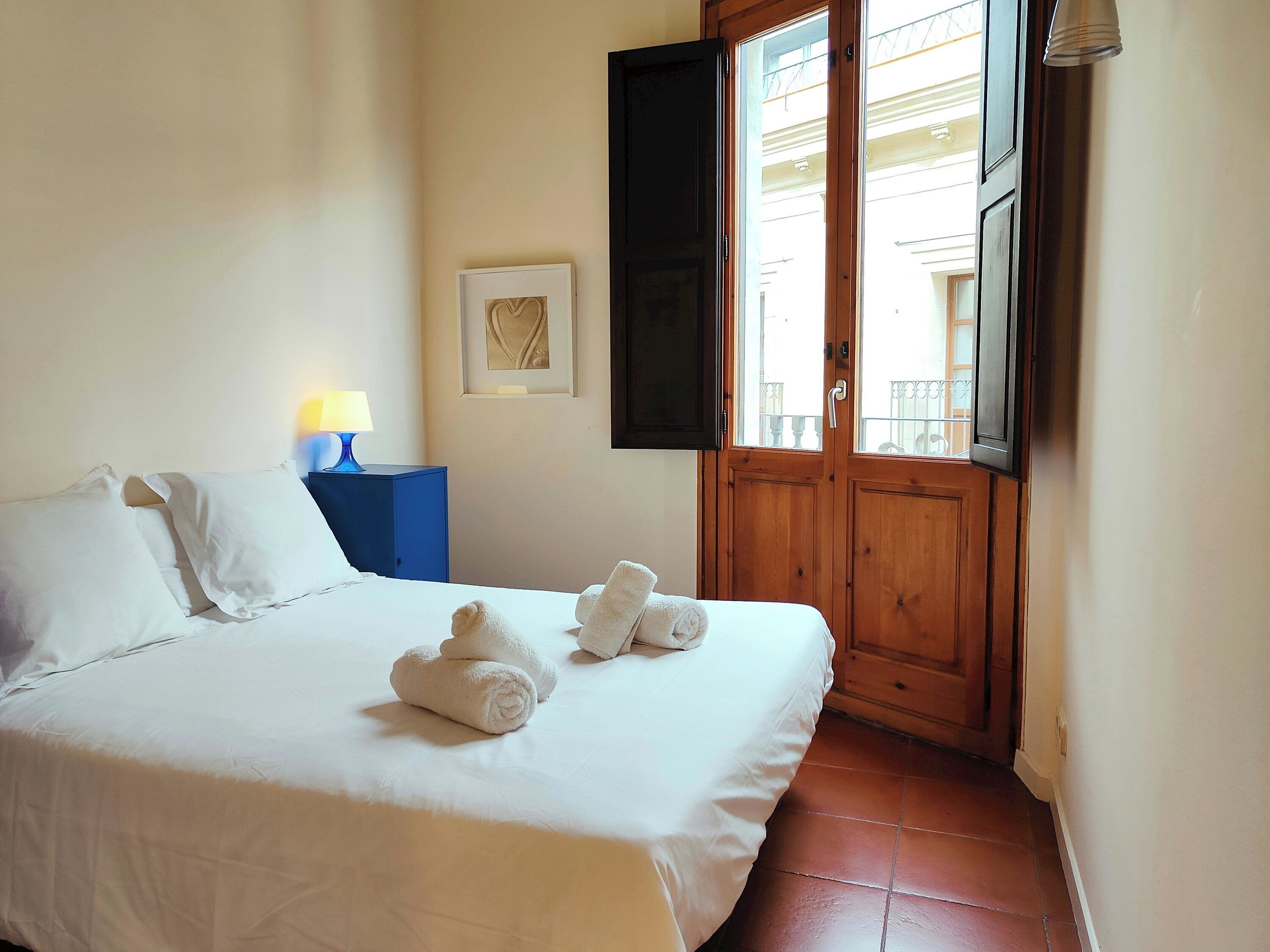 A hotel room with a bed, a nightstand, a lamp, a door, and a window.