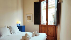 A hotel room with a bed, a nightstand, a lamp, a door, and a window.