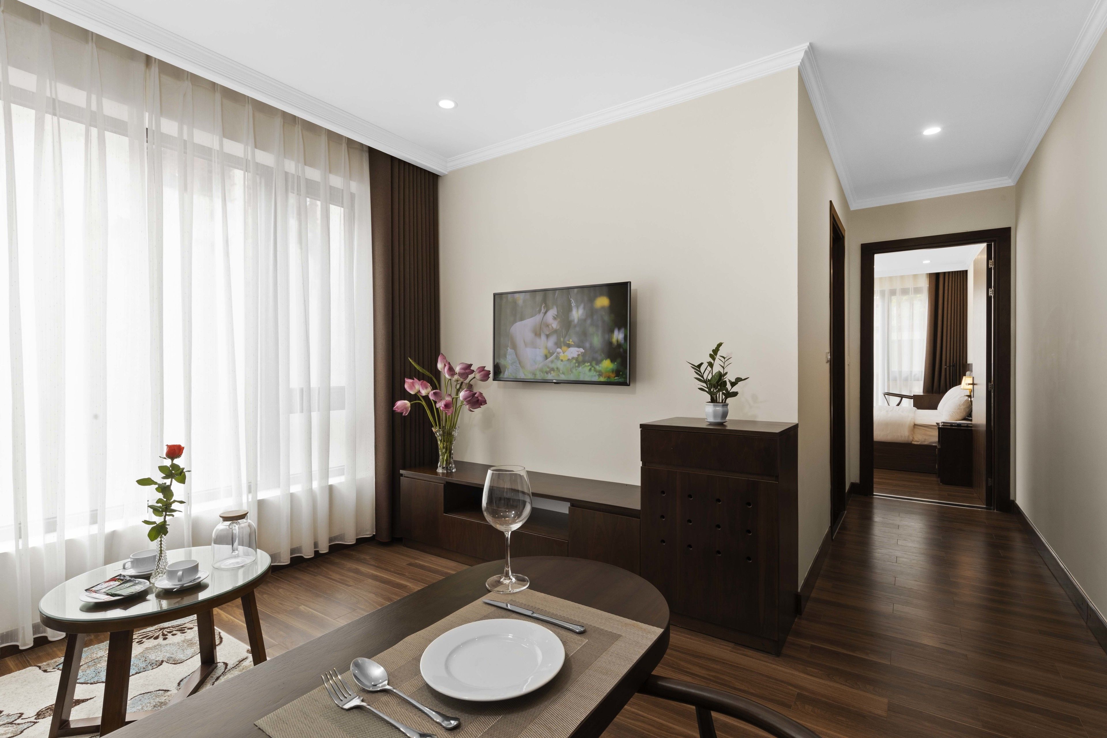 A hotel room with a dining area, a bed, a TV, and a view of the hallway.