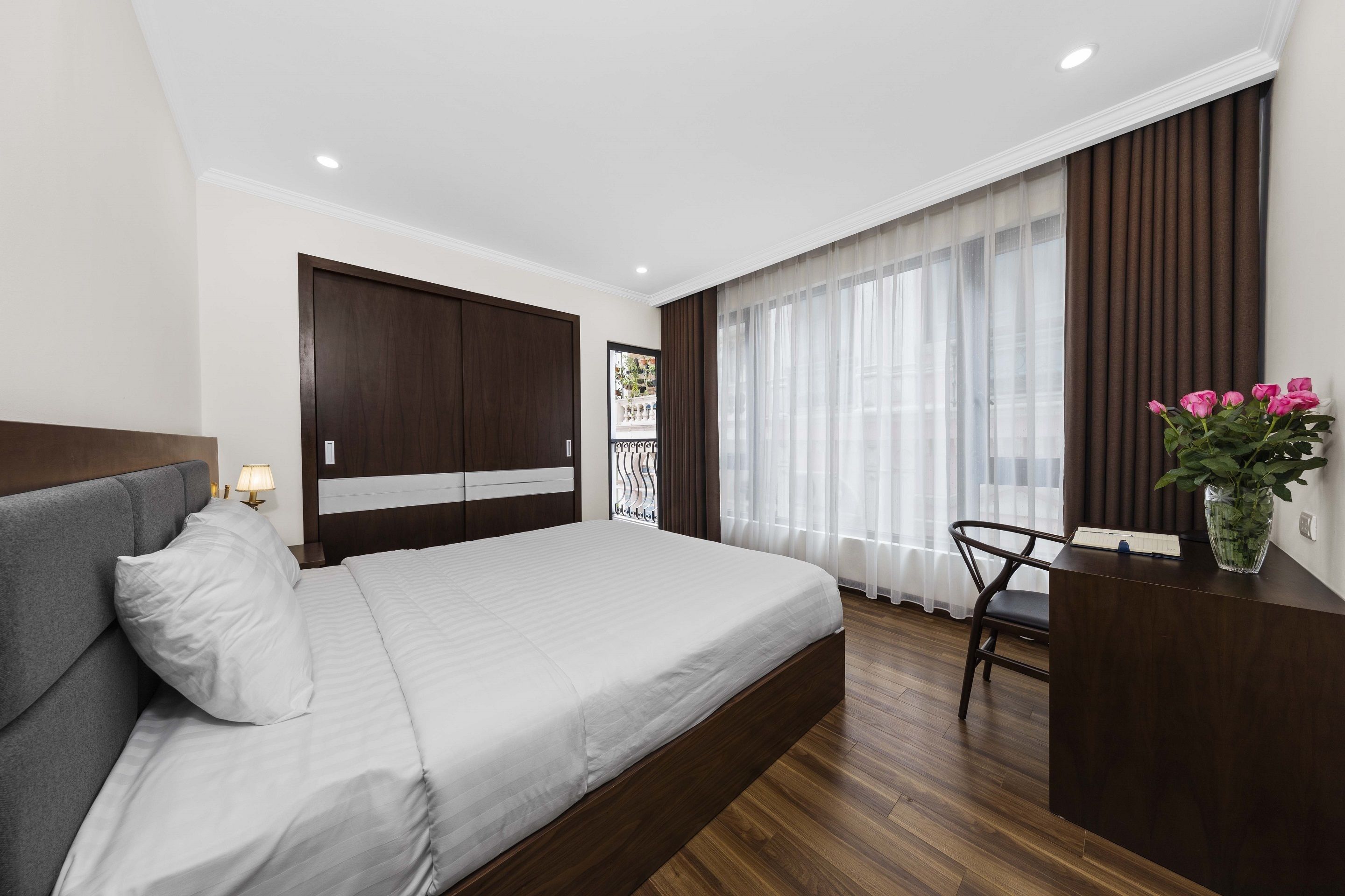 Une chambre à coucher avec un lit, un bureau, une chaise, une fenêtre avec des rideaux et une plante.