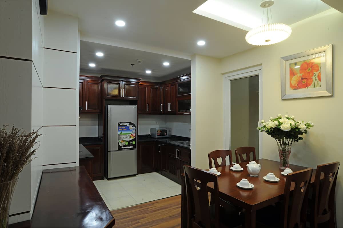 A modern kitchen with dark wooden cabinets, a refrigerator, and a dining table set with white dishes.