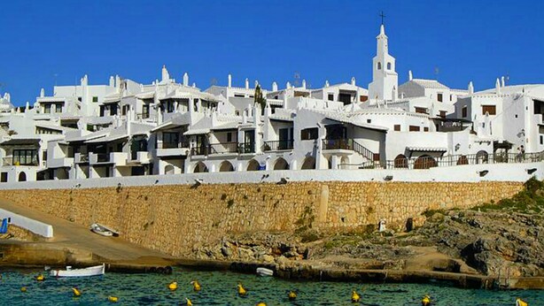 A coastal town with white buildings, a stone wall, and a clear blue sky. - 4 bedrooms Villa with pool, Sea view - 3 min walk to Binibeca vell (Binibequer)
