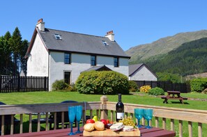 A two-story house with a white exterior and grey roof, surrounded by a well-maintained lawn and a wooden fence. - Luxury property sleeping 14 with extensive garden, sauna and hot-tub near Dunoon (Ardentinny)