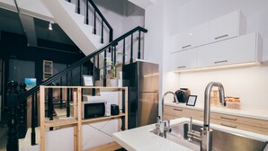 Una cocina moderna con un refrigerador de acero inoxidable, una escalera de madera y una encimera blanca.