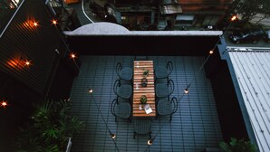 Terraza en la azotea con una mesa de madera y cuatro sillas, rodeada de luces colgantes.