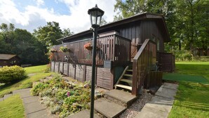 Une cabane en bois avec une véranda, des marches et un panier à fleurs suspendu.