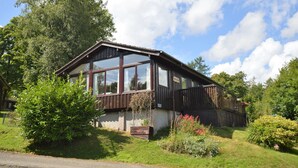 Une cabane en bois dotée de grandes fenêtres, entourée d’une végétation luxuriante et sous un ciel dégagé.