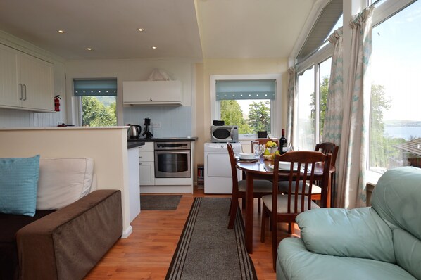 A compact kitchen with modern appliances, a dining area with a table and chairs, and a view of the outdoors. - Open plan lodge with stunning views, near Dunoon, sleeps 4, pet friendly (Hunters Quay)