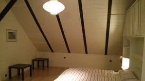Une chambre avec un plafond en pente, un lit avec une literie à rayures, une petite table et un luminaire suspendu.